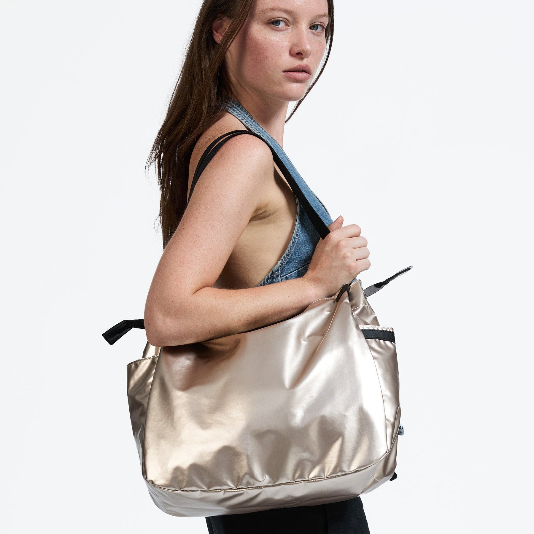 Woman carrying a large metallic gold bag on a white background