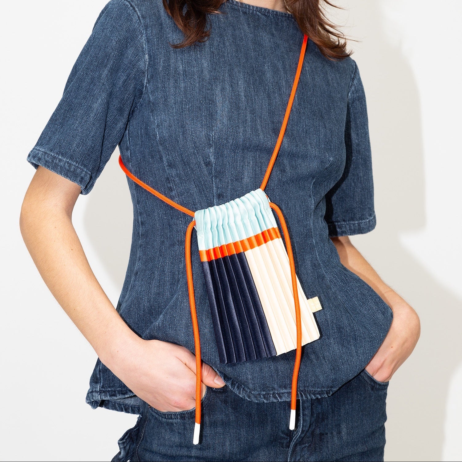 Woman wearing a denim top with a colorful bag over her shoulder against a white background