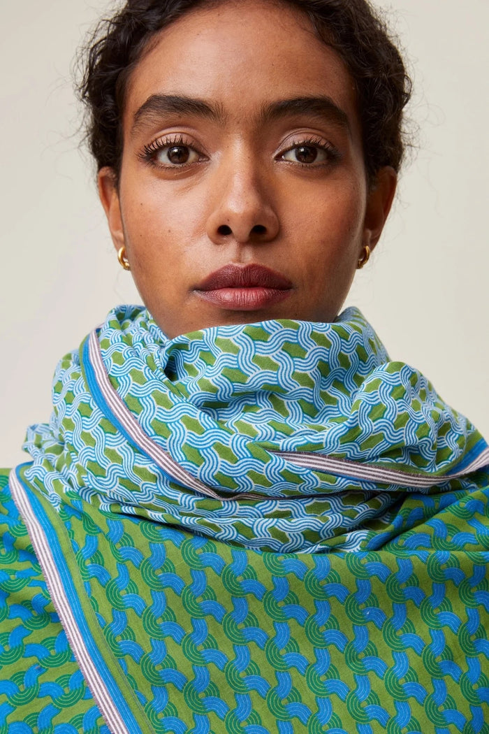 Blonde haird woman against a beige background looking away from camera with dark red Mois Mont scarf around neck 