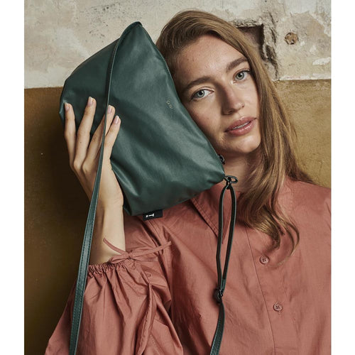 Model in silky fabrics against beige background, beige top and teracotta colour skirt with coral coloured vegan leather handbag