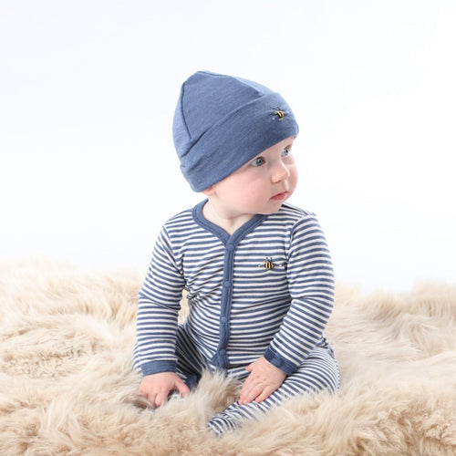 Baby in blue and white stripe onesie and bue hat sitting on fluffy rug