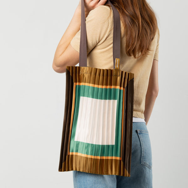 Person holding a colorful tote bag with a white square design on a plain background