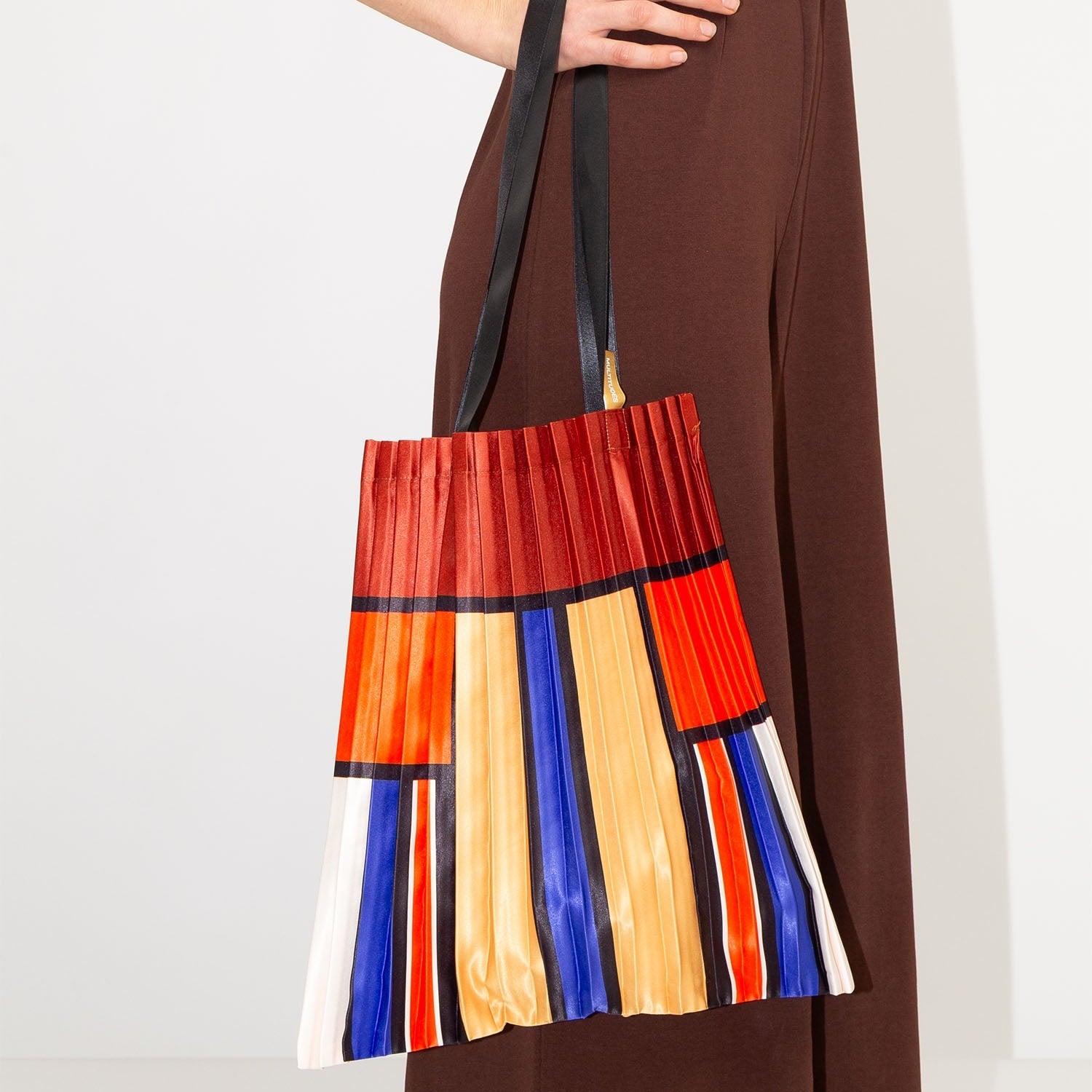 Colorful striped handbag held by a person wearing a brown dress on a white background