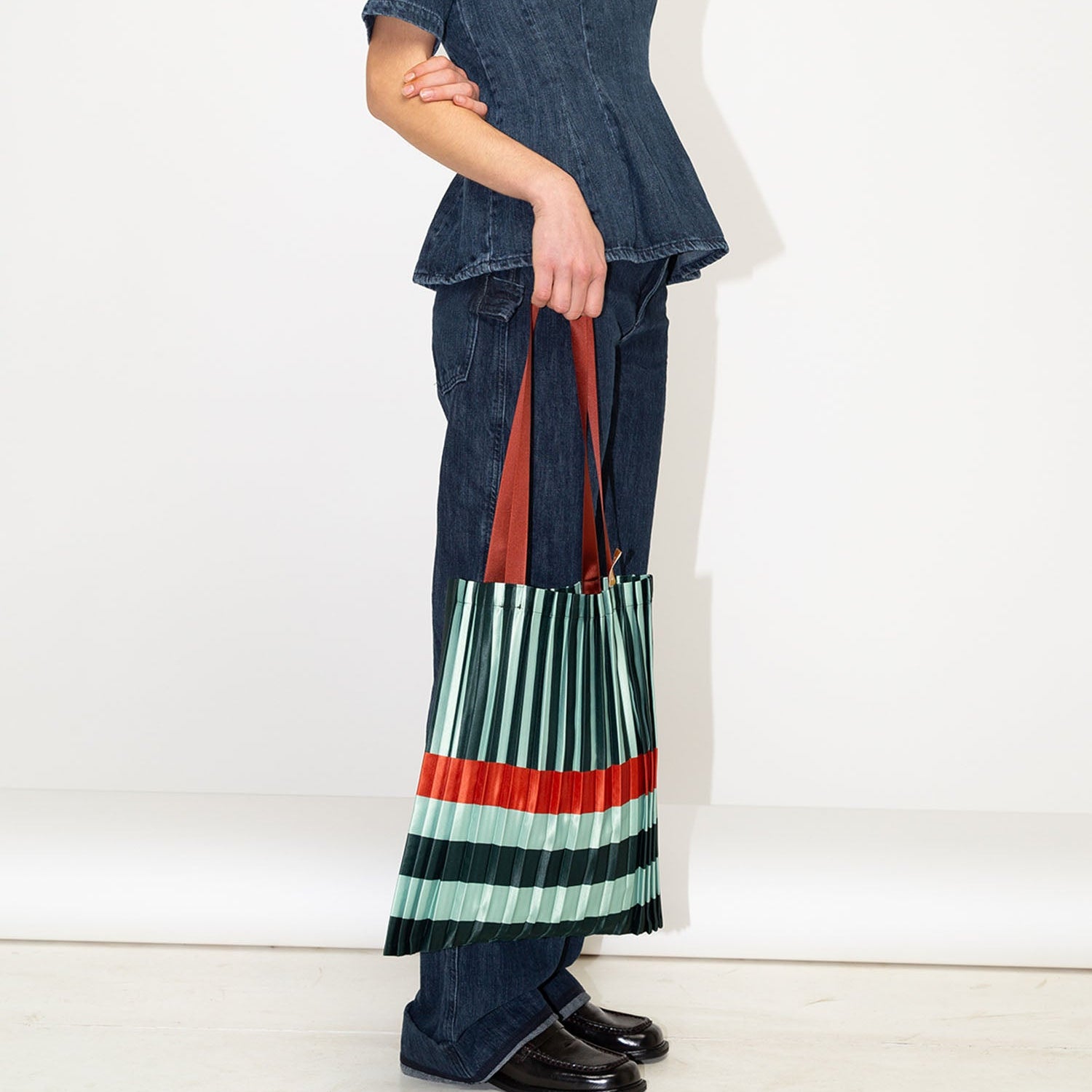 Woman wearing a denim outfit with a colorful pleated bag on a white background