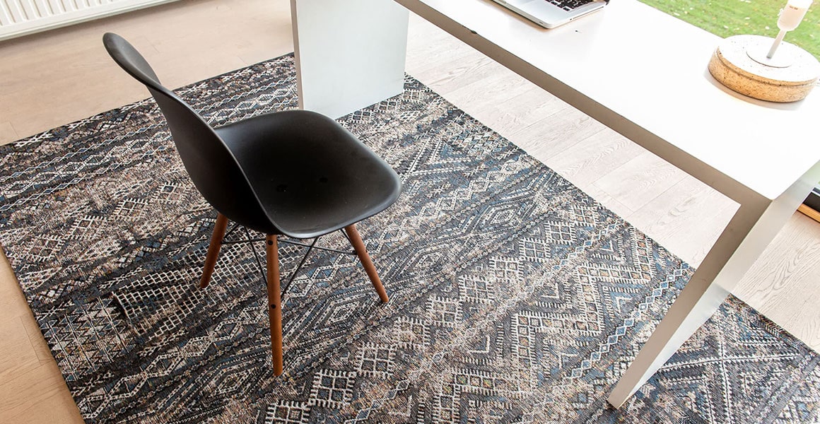 Underneath desk on wooden floor view of rug with Morrocan nomad pattern in grey and blue muted tones.